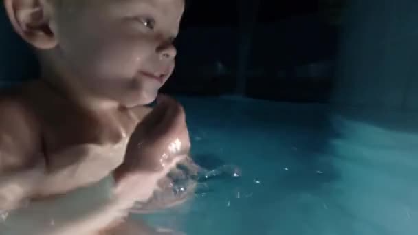 Счастливая молодая мать держит маленького сына на руках, улыбается и играет с ним в бассейне . — стоковое видео