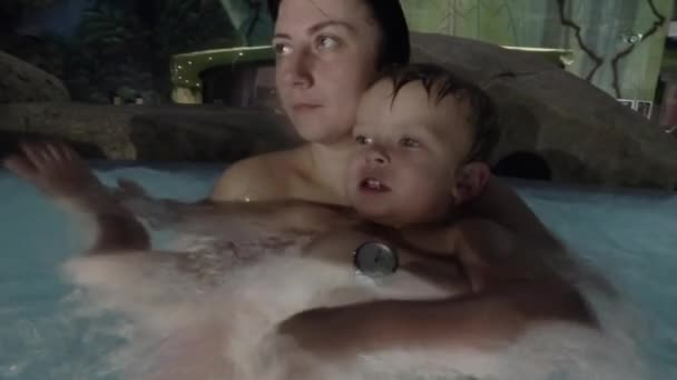 Счастливая молодая мать держит маленького сына на руках, улыбается и играет с ним в бассейне . — стоковое видео