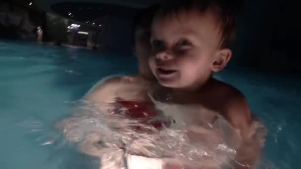 Felice giovane madre che tiene il bambino sulle braccia, sorridendo e giocando con lui in piscina . — Video Stock