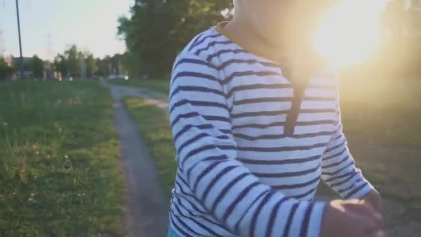 Gelukkig kind runing naar de camera op het groene gras en glimlachen. Kleine jongen zijn eerste stappen op een vers gras in een stadspark. Op het gebied van witte paardebloemen — Stockvideo