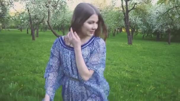 Молодая женщина бежит в яблоневом саду в весенних цветах белого цвета. Портрет красивой девушки в вечернем фруктовом саду . — стоковое видео