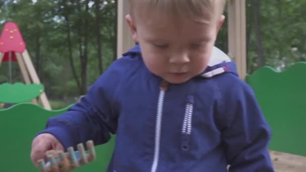 Jeux pour enfants. Petit garçon creusant dans le bac à sable. Souriez et touchez le sable . — Video