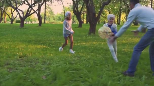 Pais e duas filhas brincando com bola no parque primaveril no pomar florescente. Lazer ativo . — Vídeo de Stock