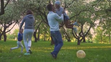 Mutlu aile çimlere sarılma. Anne ve iki kızı park çimenlikte kucaklayan. Çiçekli meyve bahçesi.