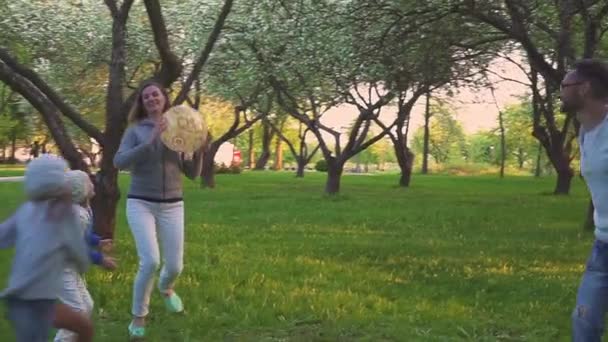 Föräldrar och två döttrar leker med bollen i vår park i blommande fruktträdgård. Aktiv fritid. — Stockvideo