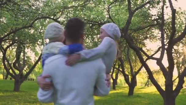 Familia feliz abrazándose en la hierba. Los padres y sus dos hijas se abrazan en el césped del parque. Huerto con flores . — Vídeo de stock