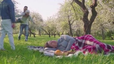 Mutlu aile piknik çiçek açması elma ağacının yakınında saat harcıyor. Anne çim, çocuk ve kocası onunla çalıştırmak yatıyor. Herkes anne kisses.