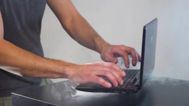 Adamın elleri ve parmakları kırılmış dizüstü bilgisayarda. Odada duman.