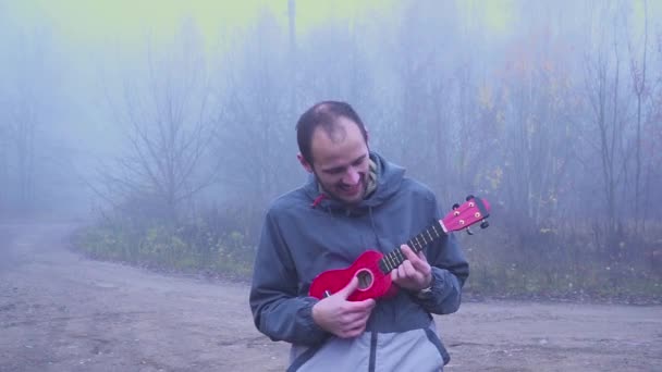 Knappe man portret spelen bas ukulele in het park, muziek concept. — Stockvideo