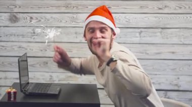 Yakışıklı adam Santa simgesi olan bir dizüstü kullanıyor ve maytap ateşle sevinir