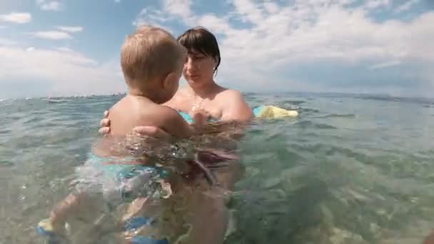 Junge Mutter schwimmt und spielt mit männlichem Kind Junge im Meer oder Meerwasser sonnigen Tag im Freien auf natürlichem Hintergrund. — Stockvideo