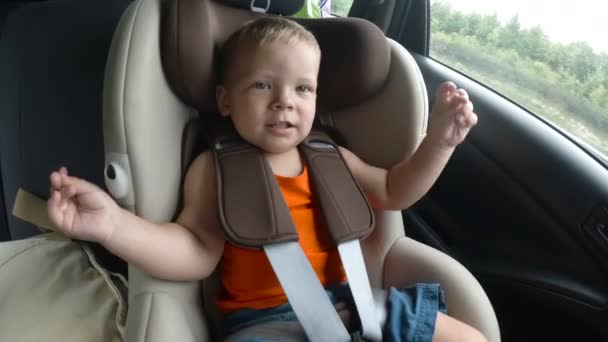 Menino na cadeirinha das crianças no carro. Kid sorri, ri e acena suas mãos alegremente . — Vídeo de Stock