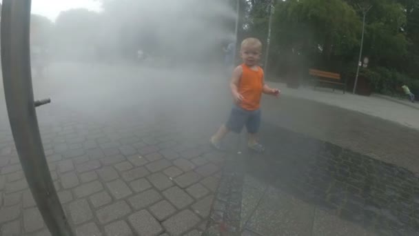 Возбужденный мальчик веселится между брызгами воды, в фонтане. Лето в городе — стоковое видео