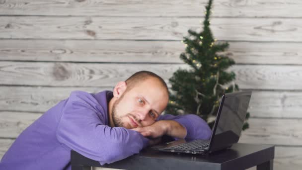 大晦日にオフィスで青年実業家を疲れています 事務所のクリスマス ツリー 机の上のノート パソコン ビジネス コンセプトです 黒いスーツを着た男 新しい年を祝います デジタル — ストック動画