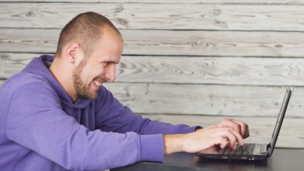 Hombre sonriente sentado en la oficina y trabajando en el ordenador portátil — Vídeos de Stock