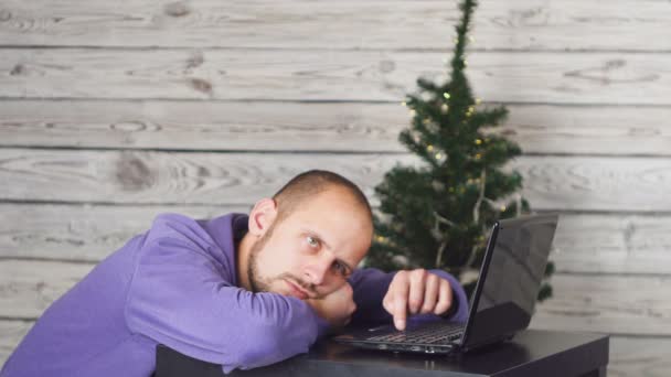 Müde schläfrige Geschäftsmann im Amt an Silvester. Weihnachtsbaum im Amt. Laptop auf Schreibtisch. Geschäftskonzept. Mann im schwarzen Anzug. Neujahrsfeiern. mit digitalem Gerät. junger Mann. — Stockvideo