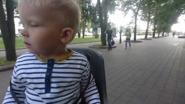 Criança menino sentado na cadeira de bicicleta enquanto dirige e olhando ao redor — Vídeo de Stock