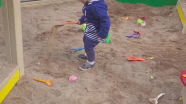 Çocuk oyunları. Kum havuzunda kazma bebeğim. Gülümsüyor ve kum dokunur.