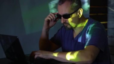 Karanlık bir odada güneş gözlüklü bir adam hacker program kodu ile çalışır. konsepti üzerine siber suçlar