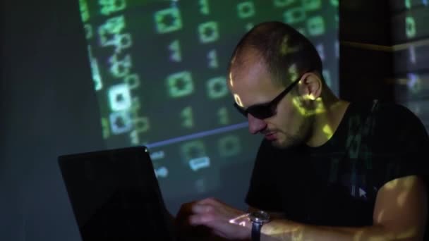 暗い部屋でサングラスの男のハッカー プログラムのコードで動く — ストック動画