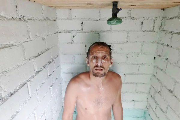 Duştaki su kesildikten sonra kaygılı beyaz köpüklü genç adam. Duş arızası ya da sıcak su kesintisi.