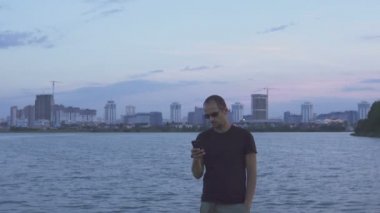 Esmer yakışıklı yürür, onun smartphone akşam şehrin arka plan üzerinde kullanır.