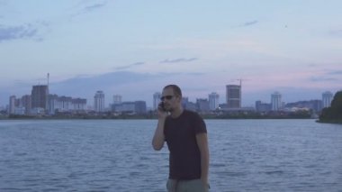 Esmer yakışıklı yürür, onun smartphone akşam şehrin arka plan üzerinde kullanır.