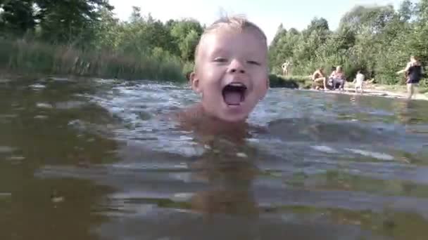 Glad liten pojke att göra stänk i vatten. Barn har roligt i sjön. — Stockvideo