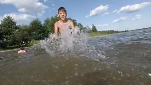 Joyeux petit garçon faisant des éclaboussures dans l'eau. Enfant s'amusant dans le lac . — Video