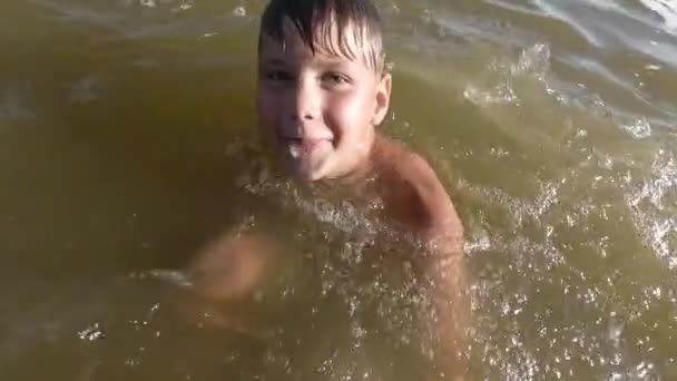 Így fröccsenő víz boldog kisfiú. Gyermeke kipróbálhassa a szórakoztató, a tóban. — Stock videók