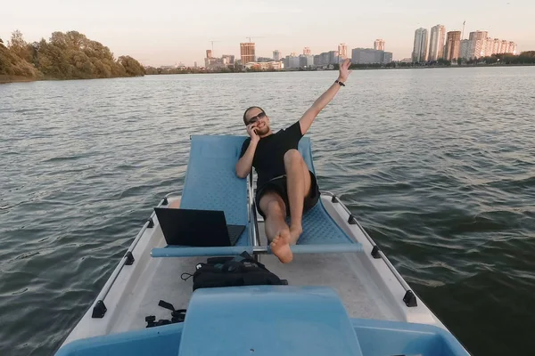 Joven freelancer trabaja en el ordenador en un barco. Negocio remoto. ganancias pasivas Imagen de archivo