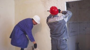 Koruyucu kıyafetli iki işçi alçı duvar yıkan.