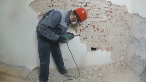 Trabalhador em terno protetor destrói parede de gesso. Trabalho sujo e duro. Equipamento de protecção individual. Capacete, respirador e óculos . — Vídeo de Stock