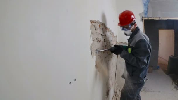 Trabajador en traje protector derriba la pared de yeso. Sucio, trabajo duro. Equipo de protección personal. Casco, respirador y gafas . — Vídeo de stock