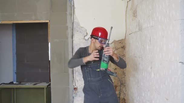 Carismático joven constructor bailando con un casco de seguridad en la azotea del edificio con un perforador en la mano . — Vídeos de Stock