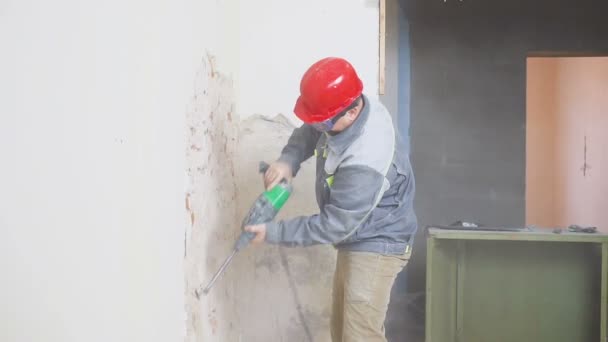 Trabalhador em terno protetor destrói parede de gesso. Trabalho sujo e duro. Equipamento de protecção individual. Capacete, respirador e óculos . — Vídeo de Stock