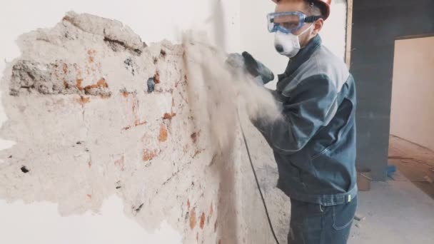 Trabajador en traje protector derriba la pared de yeso. Sucio, trabajo duro. Equipo de protección personal. Casco, respirador y gafas . — Vídeos de Stock