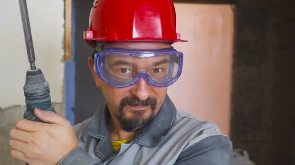 Портрет взрослого мужчины в шлеме на голове и с перфоратором в руке — стоковое видео