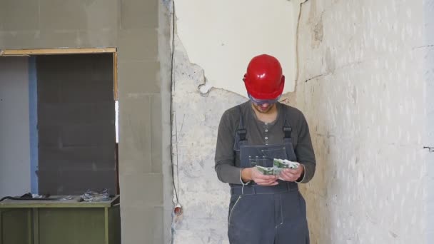 De werknemer in een constructie met helm telt geld euro tegen de achtergrond van het gerepareerde appartement. — Stockvideo