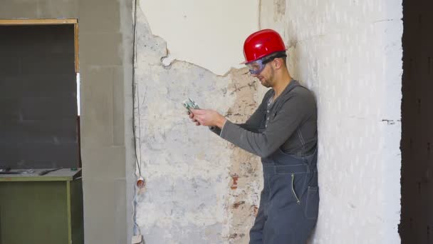 Arbetaren i en konstruktion med hjälm räknar pengar euron mot bakgrund av den reparerade lägenheten. — Stockvideo