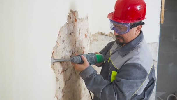 Trabajador en traje protector derriba la pared de yeso. Sucio, trabajo duro. Equipo de protección personal. Casco, respirador y gafas . — Vídeos de Stock