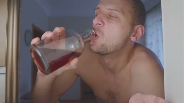 Alcoólico sem camiseta bebe álcool de uma garrafa no armário. triste em casa sofá em abuso de álcool e alcoolismo conceito . — Vídeo de Stock