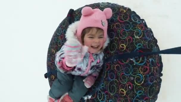 Concepto de invierno, ocio y entretenimiento - niña feliz acostada en un trineo y saludando durante el movimiento . — Vídeo de stock