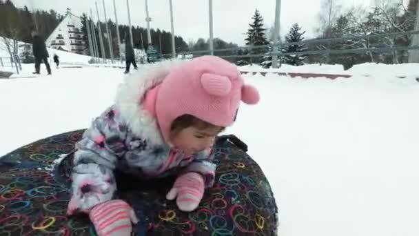 Concepto de invierno, ocio y entretenimiento - niña feliz acostada en un trineo y saludando durante el movimiento . — Vídeos de Stock