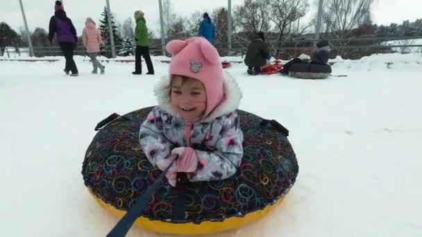 Vinter, fritid och underhållning koncept - glad liten tjej liggandes på en släde och vinkar under rörelse. — Stockvideo