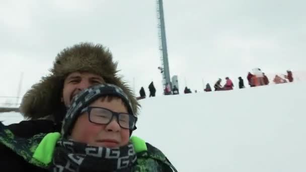 Młody człowiek z wesoły chłopiec z roller coaster jeździć w zimie na lodzie. Przystojny tata i syn, śmiejąc się w winter park. Szczęśliwa rodzina gra ze śniegu. — Wideo stockowe