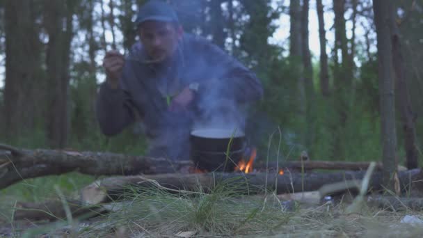 Turista hirviendo y saborea la cena de un fuego en el bosque por la noche — Vídeo de stock