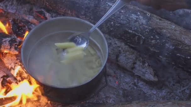 在傍晚的森林里用锅在篝火上煮面食。厨师用勺子搅动食物。特写 — 图库视频影像