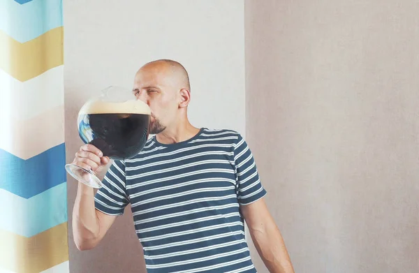 Kocaman bir bardak birası olan mutlu, genç bir adam. Güler, sevinir, sonra da içer..