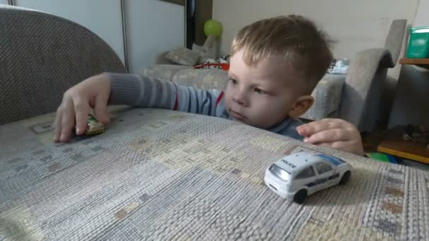 Een kleine babyjongen spelen met zijn speelgoed op fauteuil. Kleuter jongen speelt met speelgoedauto 's. — Stockvideo